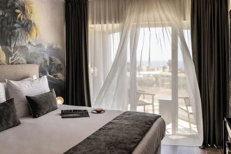 Une chambre lumineuse avec un lit fait donnant sur une terrasse et la mer.