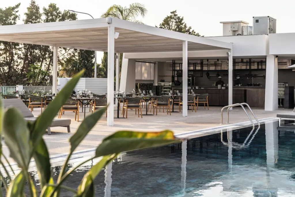 Une piscine bordée de chaises longues et d'un espace repas ombragé.