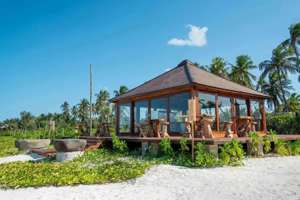Un pavillon en bois sur une plage de sable blanc, avec des sièges en bois sculpté.