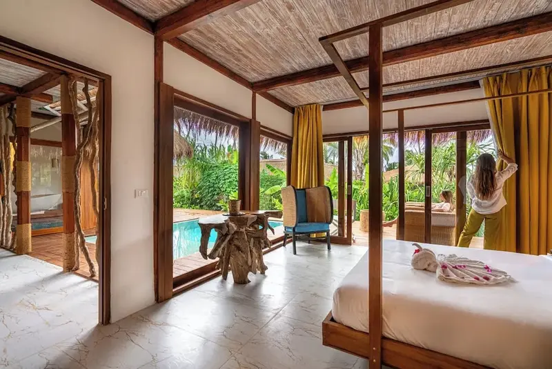 Une chambre lumineuse s'ouvre sur une piscine et une végétation tropicale.