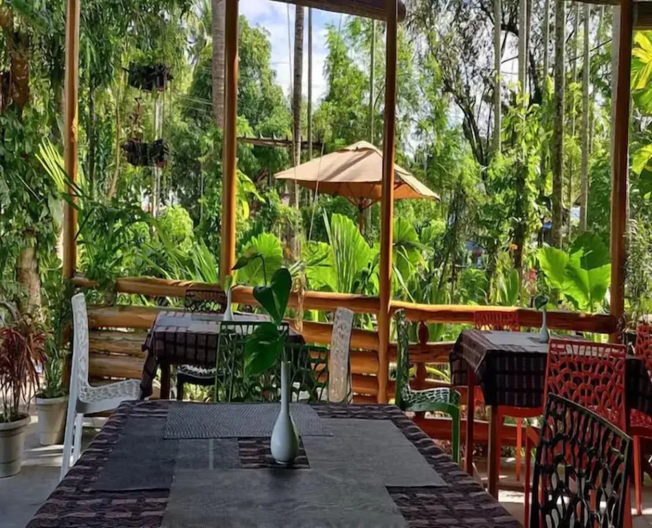 Une salle à manger extérieure ombragée s'ouvre sur une végétation luxuriante.