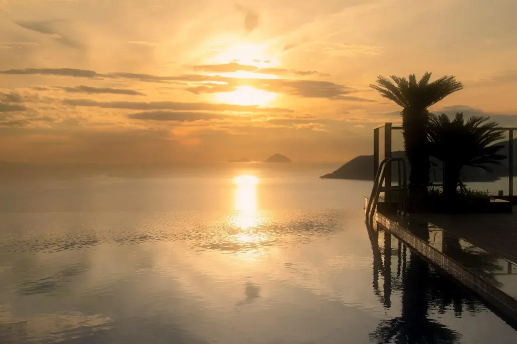 Une piscine à débordement reflète les couleurs d'un coucher de soleil sur la mer.