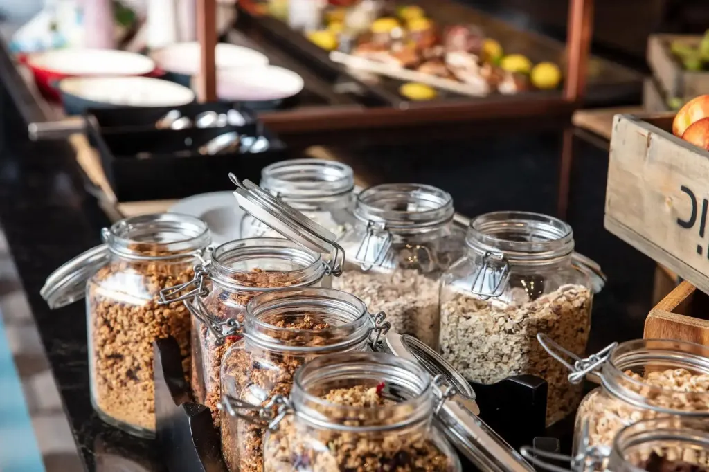 Des bocaux en verre remplis de céréales et de granola sont disposés sur un buffet.