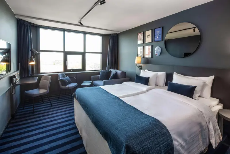 Une chambre moderne avec un grand lit et un coin salon près d'une fenêtre.
