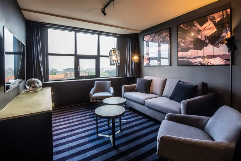 Un salon moderne avec canapé, fauteuils et une grande fenêtre donnant sur la ville.