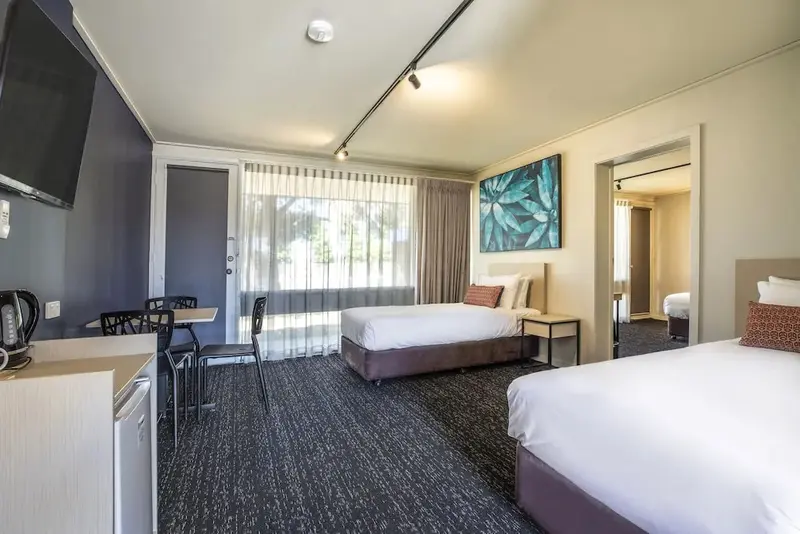 Une chambre lumineuse avec deux lits et un coin repas près d'une porte-fenêtre.