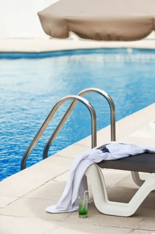 Transat et echelle en inox au bord d'une piscine ensoleillée.