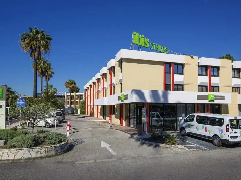 Façade d'un bâtiment moderne avec un parking et des palmiers.