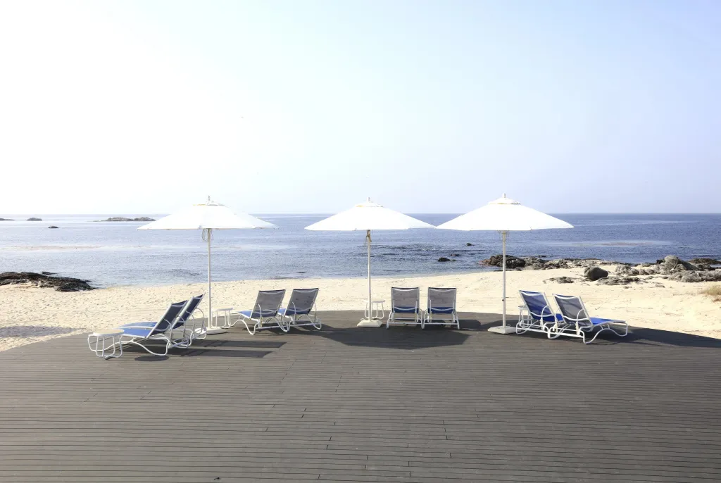 Transats blancs sous des parasols sur une terrasse en bois face à la mer.