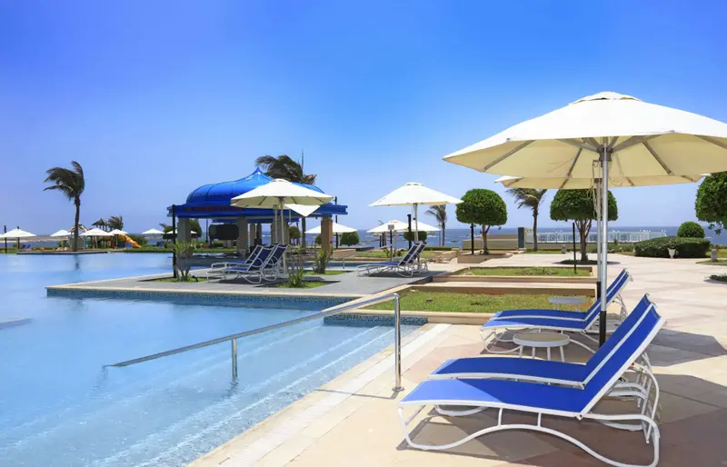 Transats bleus disposés au bord d'une piscine ensoleillée avec parasols blancs.