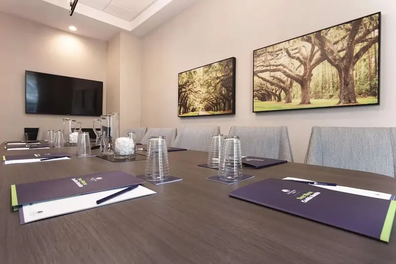 Une grande table de réunion est entourée de chaises dans une salle lumineuse.