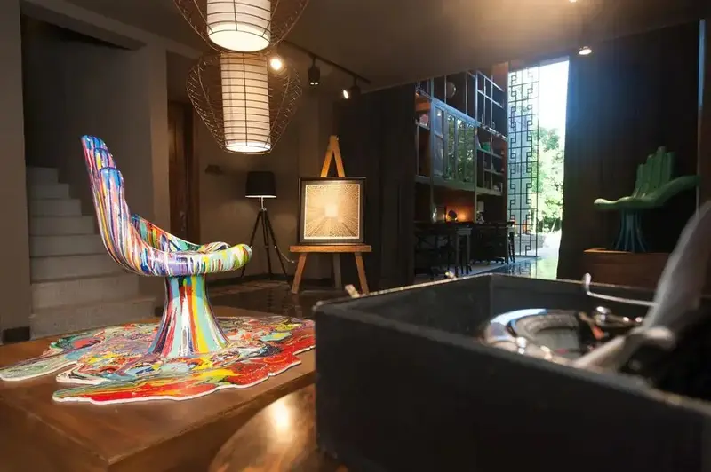 Un intérieur lumineux présente un fauteuil coloré et une œuvre d'art sur chevalet.