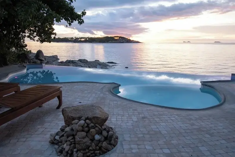 Une piscine à débordement surplombe la mer au coucher du soleil.