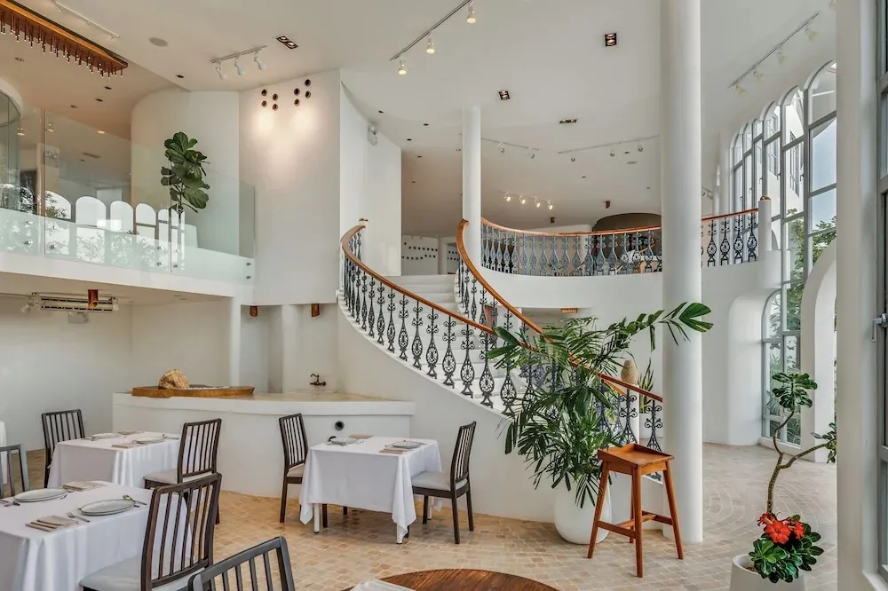 Une salle lumineuse avec des tables dressées et un escalier en colimaçon.