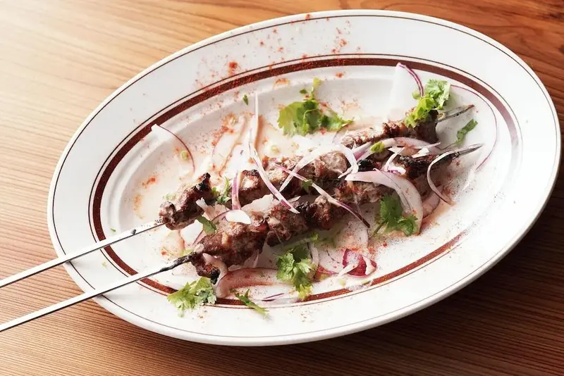 Brochettes de viande grillée servies sur une grande assiette blanche.