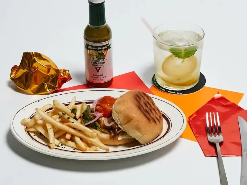 Assiette garnie d'un hamburger, de frites et d'une sauce piquante, accompagnée d'une boisson.