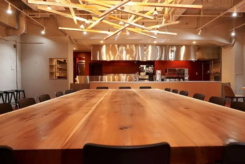 Une longue table en bois occupe le centre d'une salle lumineuse.
