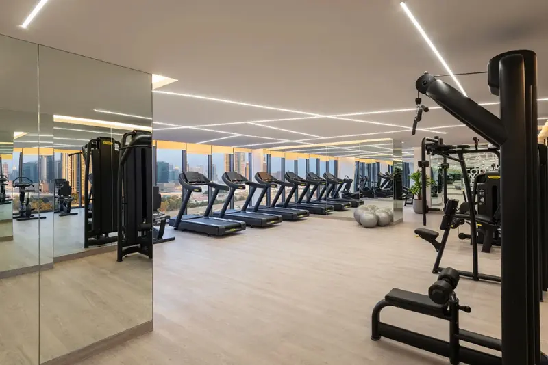 Une salle de sport lumineuse avec des équipements de musculation et des tapis de course face à une grande baie vitrée.
