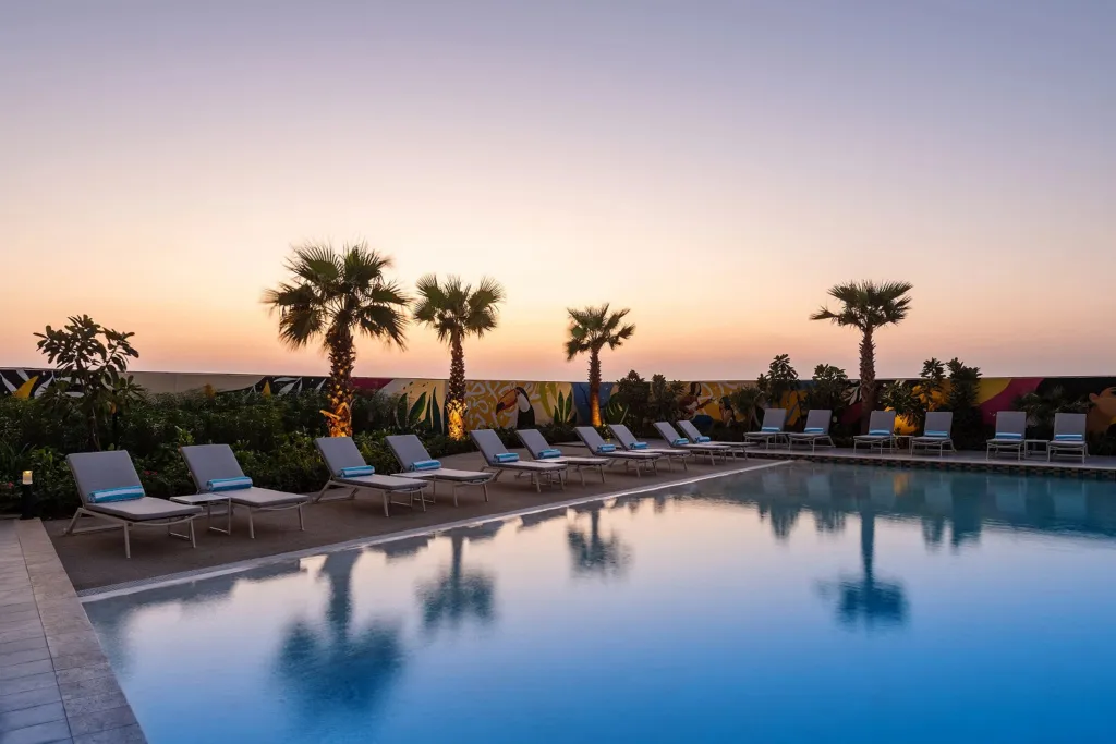 Transats alignés au bord d'une piscine illuminée au crépuscule.