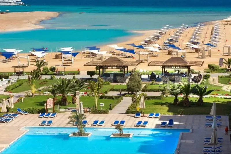 Vue aérienne d'un complexe hôtelier avec piscine, plage et parasols.