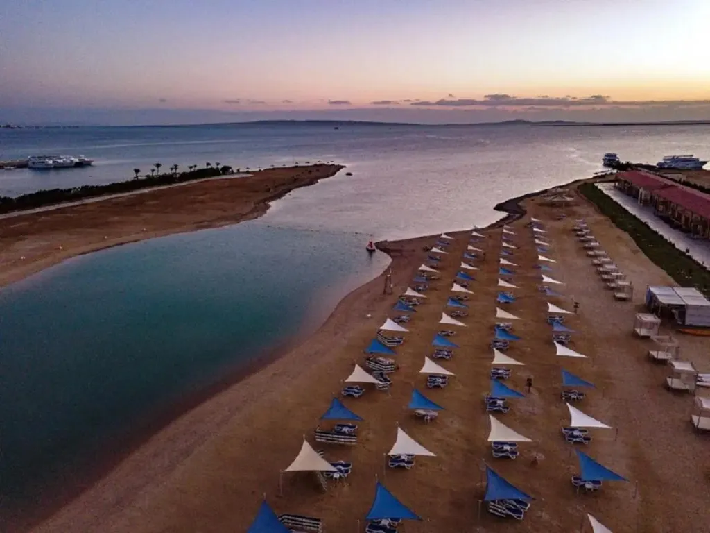 Plage de sable fin avec transats et parasols bleus au coucher du soleil.