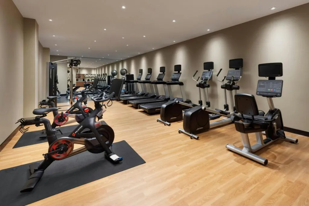 Une salle de sport lumineuse avec des équipements de fitness alignés sur un sol en bois.