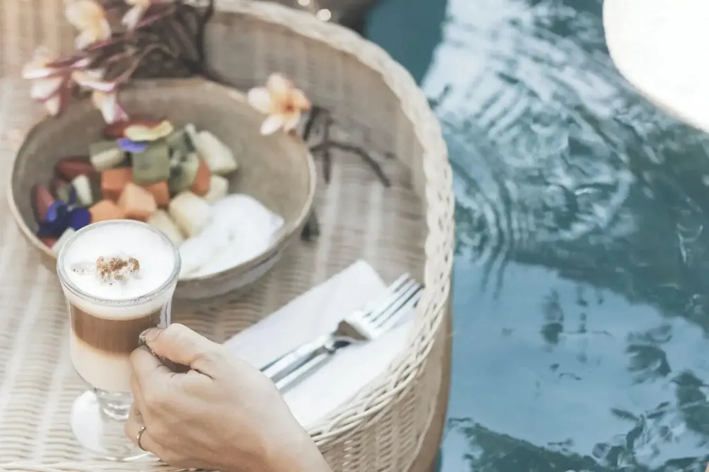 Une boisson et des fruits frais sont servis sur une table en osier au bord d'une piscine.