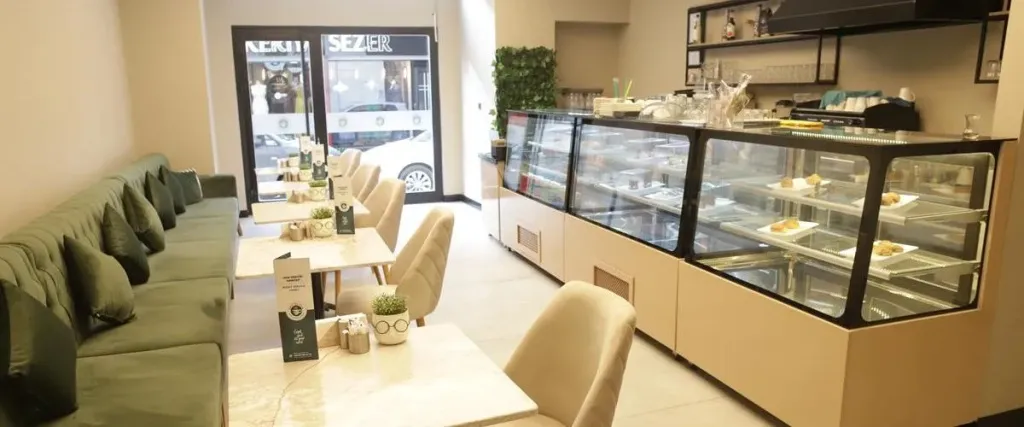 Une salle lumineuse avec des tables et des banquettes vertes, un comptoir vitré rempli de pâtisseries.