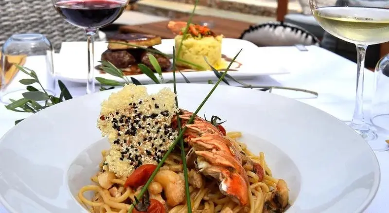 Une table est dressée avec des plats de pâtes et de viande, accompagnés de boissons.