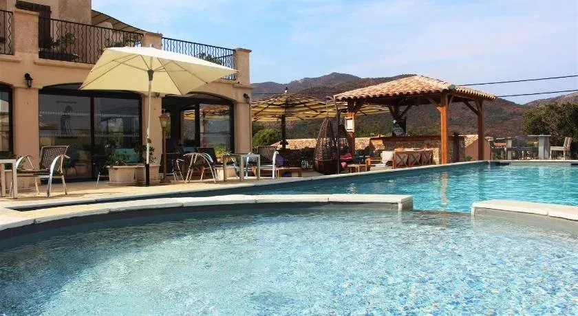 Une piscine turquoise bordée d'une terrasse ensoleillée avec des chaises longues et un espace ombragé.