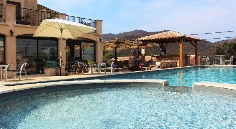 Une piscine turquoise bordée d'une terrasse ensoleillée avec des chaises longues et un espace ombragé.