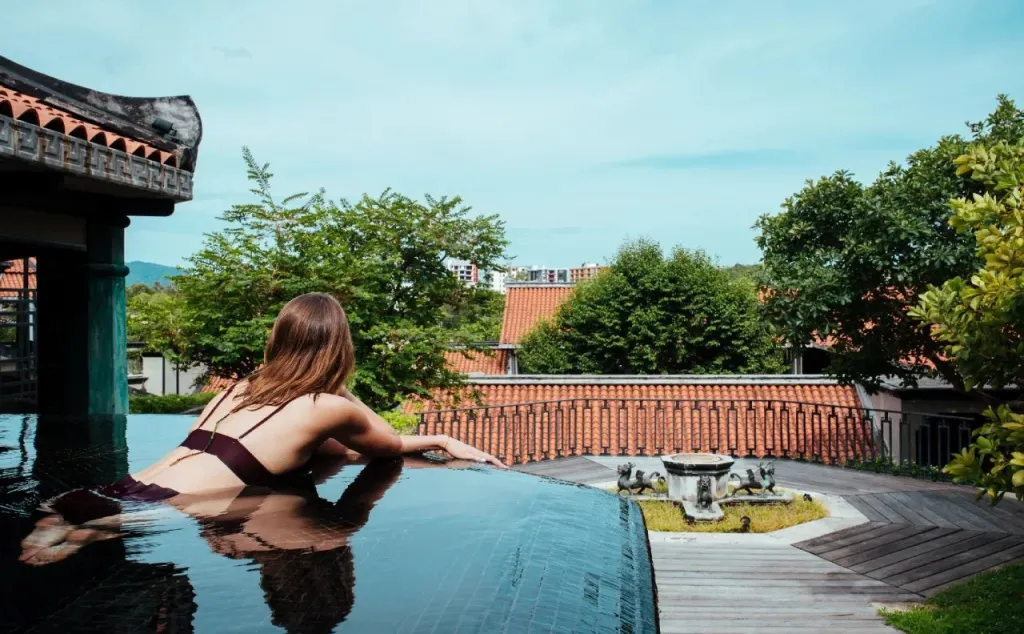 Une femme se détend au bord d'une piscine à débordement avec vue sur un jardin luxuriant.