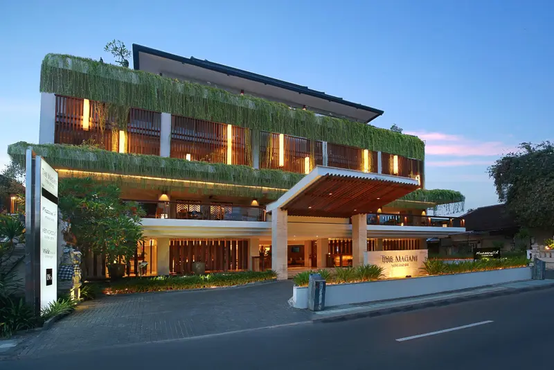 Façade moderne d'un bâtiment illuminé au crépuscule, avec une végétation luxuriante sur le toit.