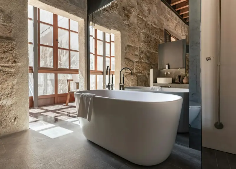 Une baignoire blanche se trouve dans une salle de bain aux murs de pierre.