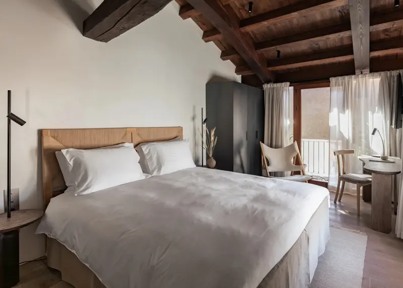 Une chambre lumineuse avec un grand lit recouvert de draps blancs et une fenêtre laissant entrevoir l'extérieur.