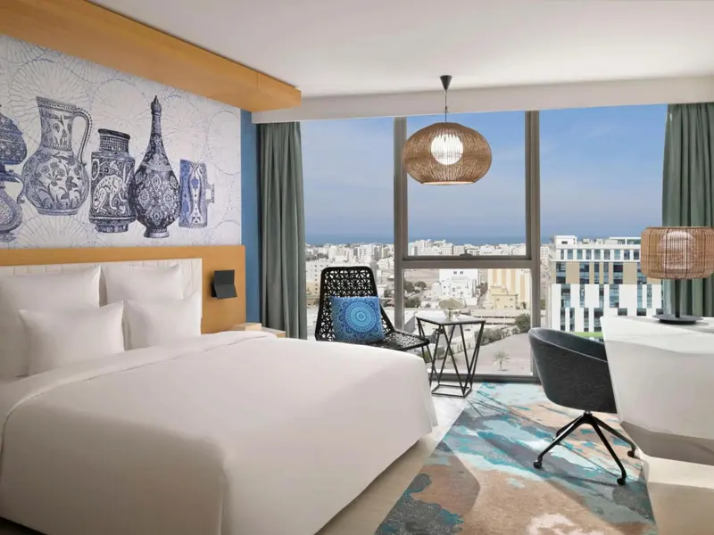 Une chambre lumineuse avec un grand lit et une vue sur la ville et la mer.