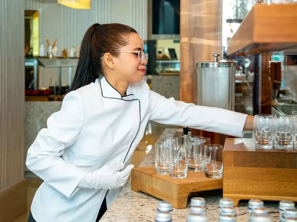 Une employée ajuste des verres sur un comptoir de buffet.