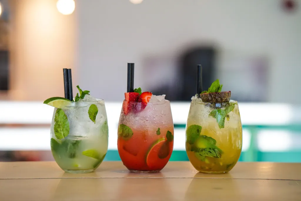 Trois cocktails colorés sont présentés sur un comptoir en bois.