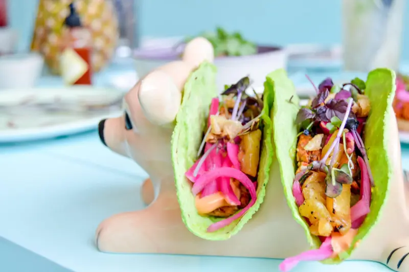 Tacos colorés servis dans un présentoir original sur une table turquoise.