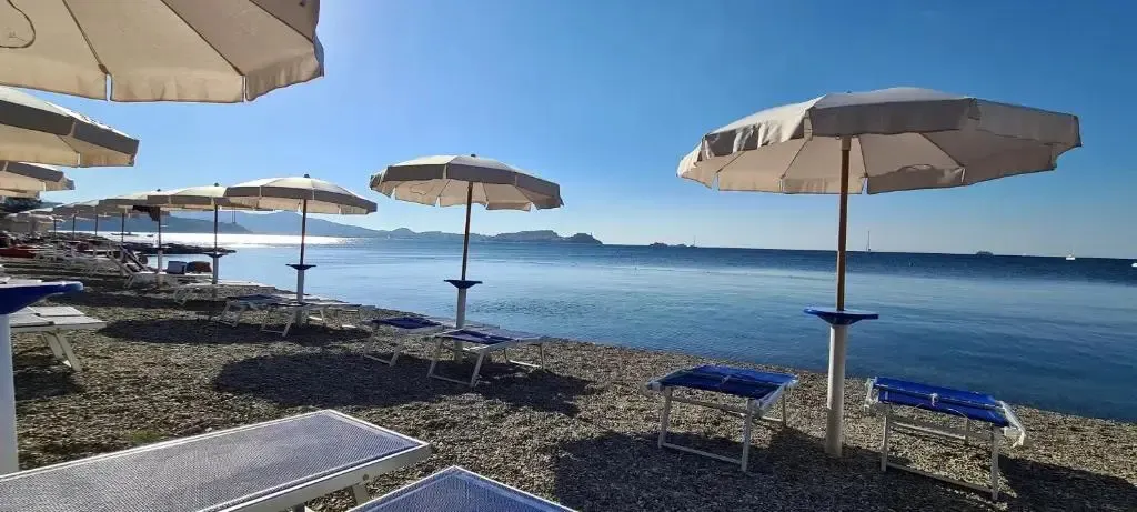 Plage de galets avec parasols et transats sous un ciel bleu.