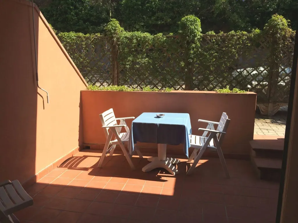 Une table et des chaises en bois sont disposées sur une terrasse carrelée.