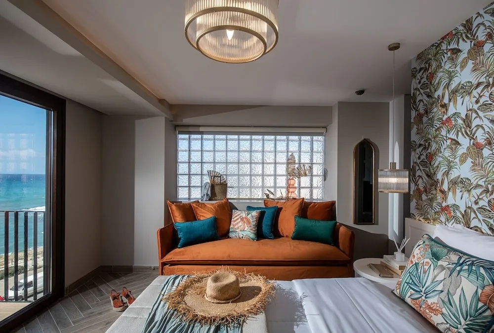 Espace de détente lumineux avec canapé orange et vue sur la mer.