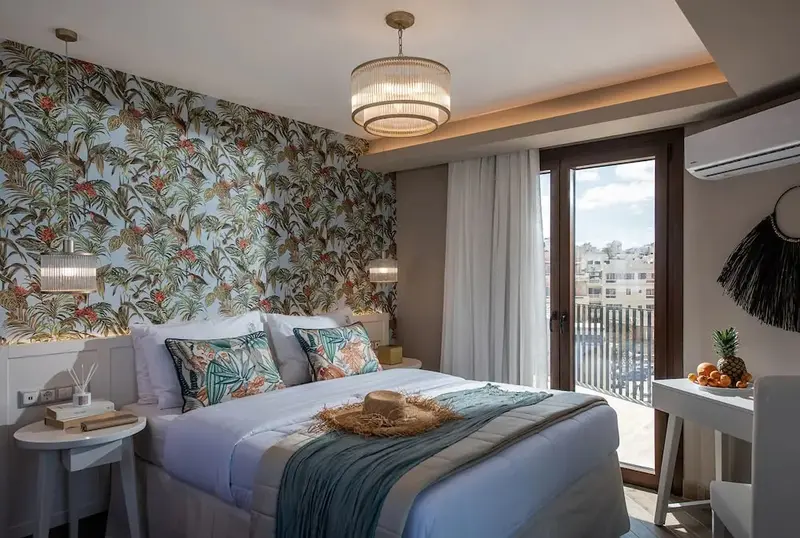 Une chambre lumineuse avec un lit recouvert d'une courtepointe blanche et de coussins colorés, donnant sur une terrasse.