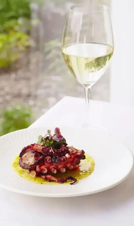 Un plat de poulpe est présenté avec un verre de vin sur une table blanche.