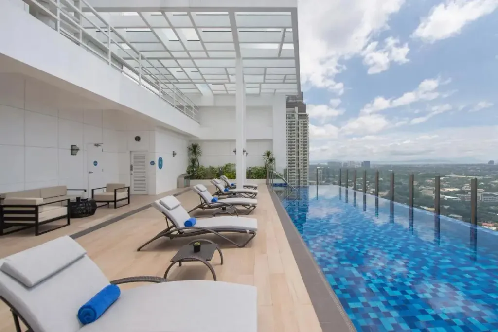 Transats blancs alignés au bord d'une piscine à débordement avec vue sur la ville.