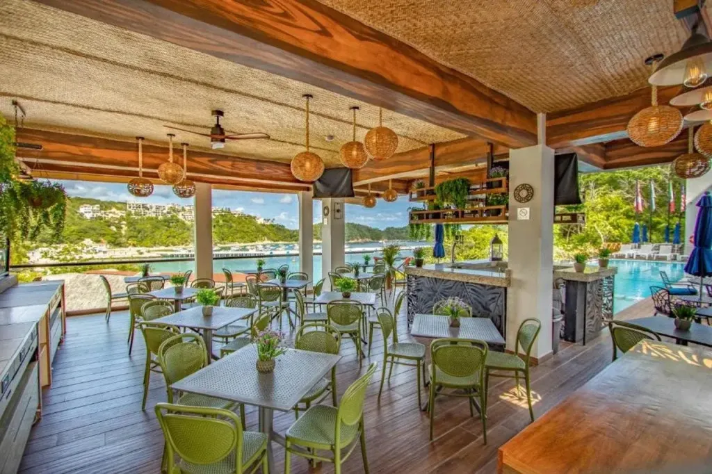 Une salle à manger lumineuse avec des tables vertes et une vue sur la mer.