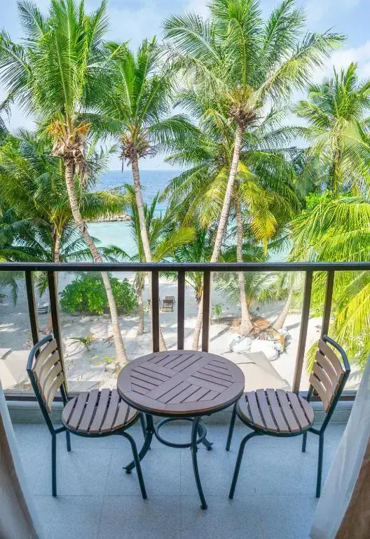 Une table et deux chaises en osier sur un balcon avec vue sur la mer et la végétation tropicale.