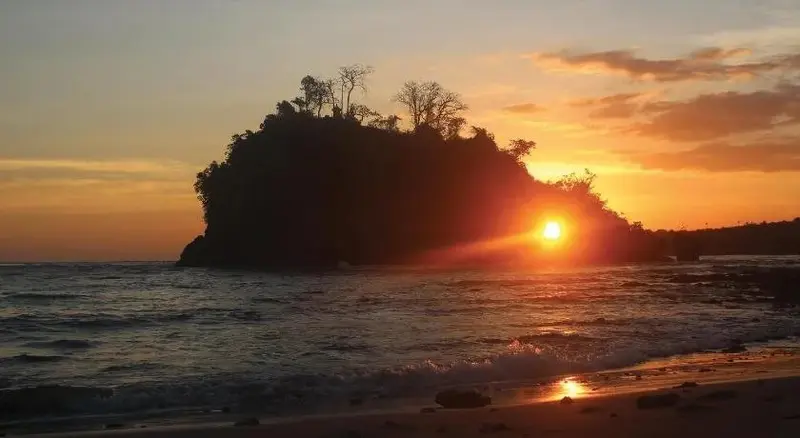 Le soleil se couche sur une île rocheuse bordée d'une plage.