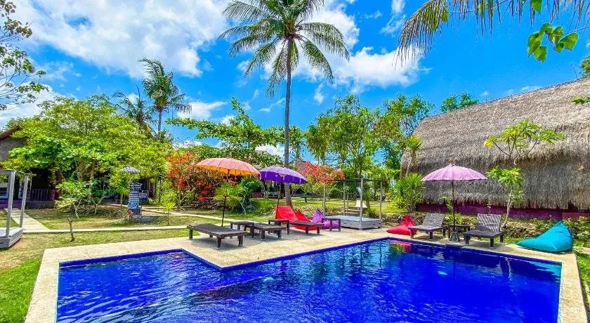 Une piscine bleue bordée de chaises longues et de parasols colorés, dans un jardin tropical.