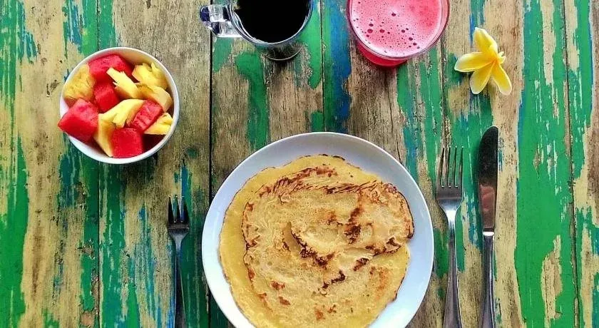 Une table colorée est dressée avec un petit-déjeuner composé de fruits frais et d'une crêpe.